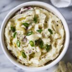 bowl of garlic mashed red skin potatoes topped with butter and green onions.