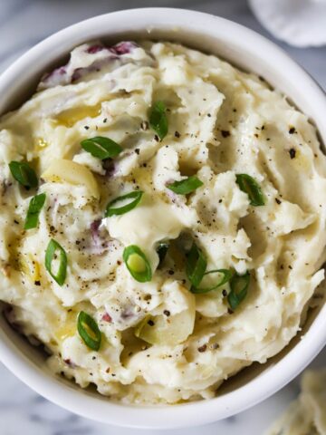 bowl of garlic mashed red skin potatoes topped with butter and green onions.