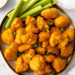 Plate of vegan buffalo cauliflower wings garnished with celery and green onions