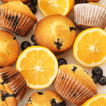 overhead shot of 9 lemon-blueberry muffins on crinkled parchment paper, blueberries and lemon rounds scattered throughout