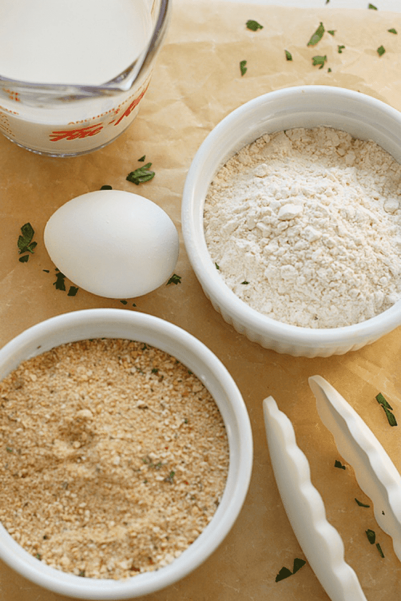 Overhead shot of milk, flour, egg , chopped parsley and breadcrumbs on a parchment background 