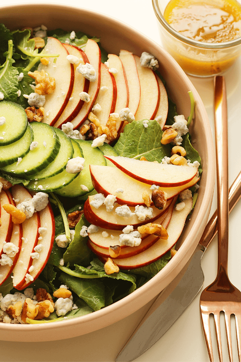 Close up view of Baby Kale and Apple Salad in shallow pink bowl with cider vinaigrette on the side