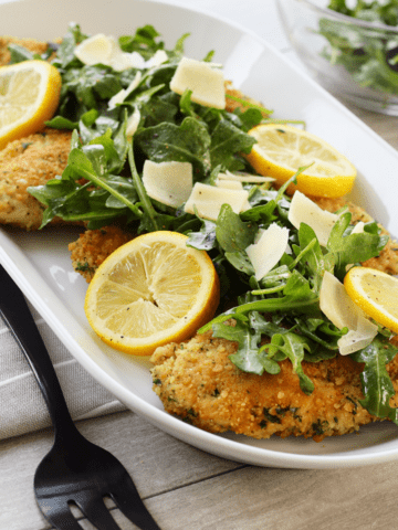 close up of breaded chicken topped with Lemon arugula salad