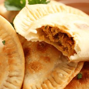 Close up of golden flaky Cape Verdean pastel that has been bitten to show flaky seasoned tuna on the inside.