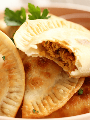 Close up of golden flaky Cape Verdean pastel that has been bitten to show flaky seasoned tuna on the inside.