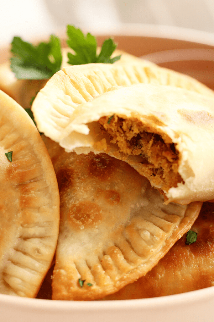 Close up of golden flaky Cape Verdean pastel that has been bitten to show flaky seasoned tuna on the inside.