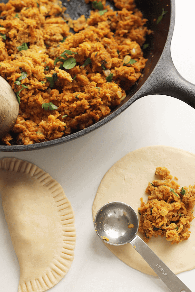 Overhead shot of browned and seasoned Cape Verdean Tuna, one pastel that's been filled and pressed and an emanada disc with 2 measured teaspoons of tuna filling. This photo is meant to show the viewer how Cape Verdean pastel is assembled.