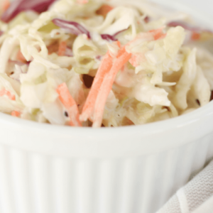 This is a close-up shot of creamy sweet and tangy coleslaw in a white ramekin. The purpose of the photo is to entice the reader.