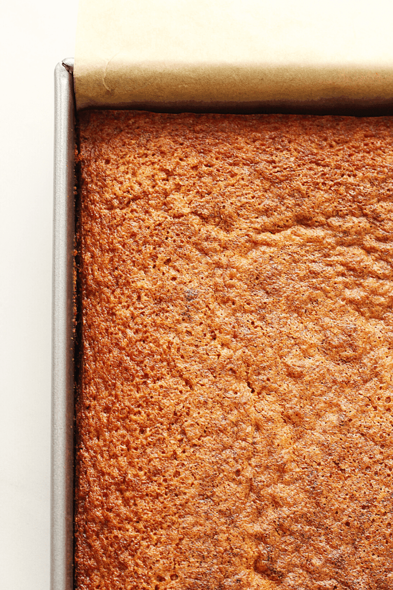 close up photo of unfrosted carrot cake in a 9x13 metal baking pan lined with sheet of parchment