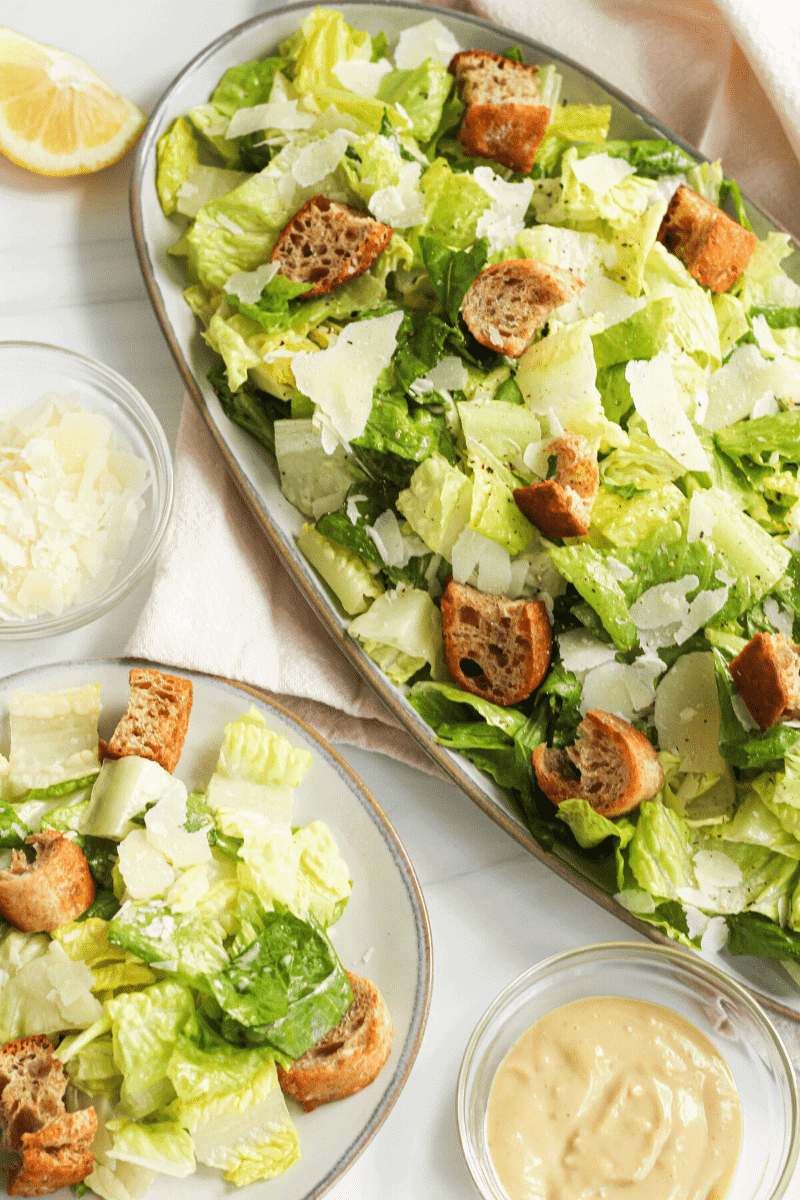 This is an overhead shot of a caesar salad made with romaine lettuce leaves, whole grain croutons and shaved parmesan tossed in homemade caesar dressing. The purpose of the image is to entice the reader and suggest how to plate and serve.