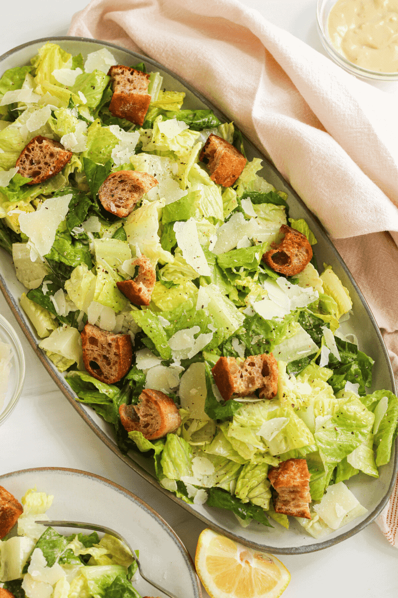 This is an overhead shot of a caesar salad made with romaine lettuce leaves, whole grain croutons and shaved parmesan tossed in homemade caesar dressing. The purpose of the image is to entice the reader and suggest how to plate and serve.