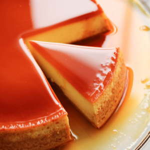 Overhead shot of sliced Cape Verdean pudim (flan) on a clear plate topped with glossy caramel syrup. The purpose of this image is to entice and show the reader how to slice the reader.