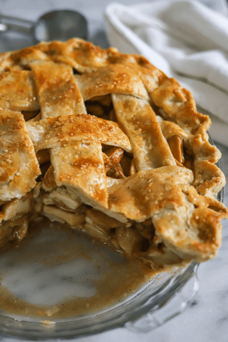 This is a close up of the classic apple pie that's been sliced. A very small amount of the liquid from the filling is pooled on the bottom of the glass pie plate, and the lattice crust is a deep golden brown.