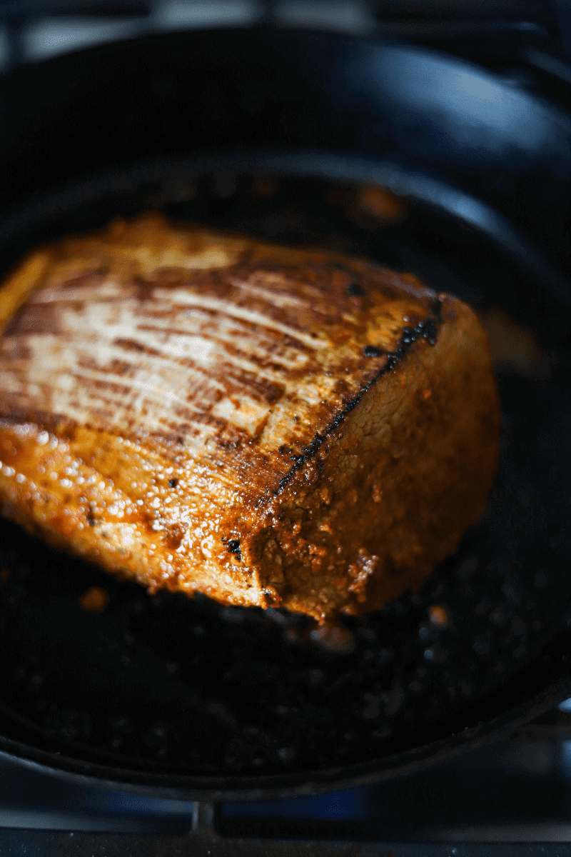 Close up photo of seared beef top-round roast (used to make Mexican birria) in a cast iron skillet)