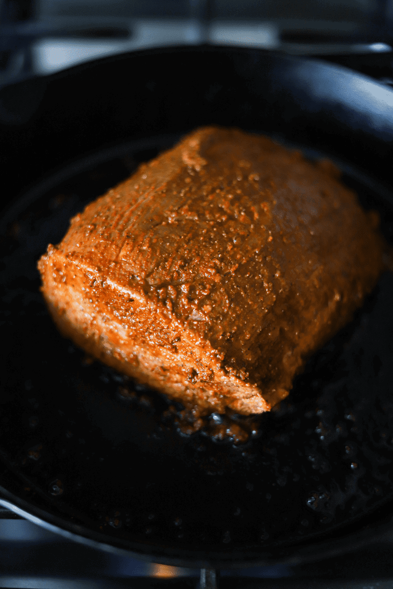 Close up photo of a beef top-round roast (used to make Mexican birria) being seared in a cast iron skillet