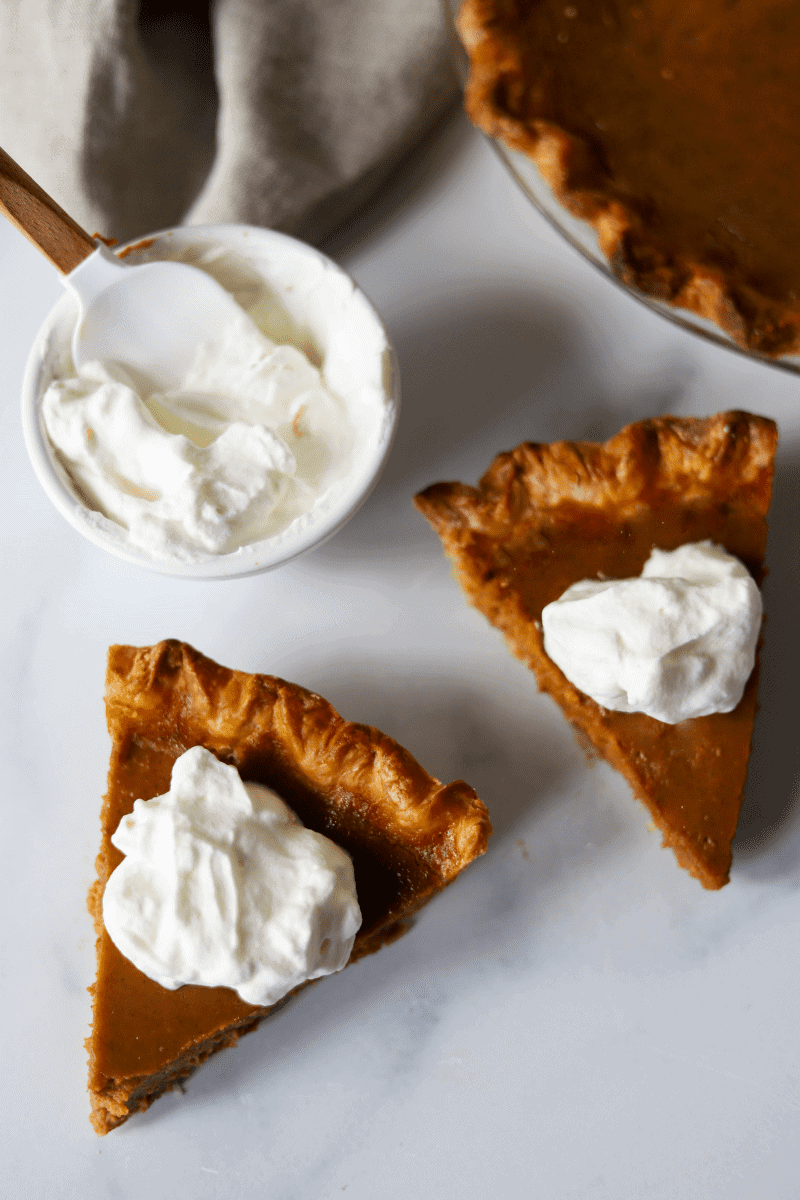 slices of pumpkin pie topped with dollops of whipped cream.  The pie dish is in the background and a dish of whipped cream is off to the side.