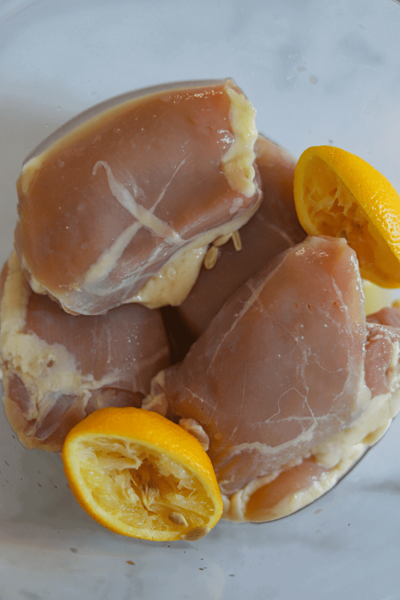 Close up of uncooked chicken thighs in a bowl with squeezed lemon halves