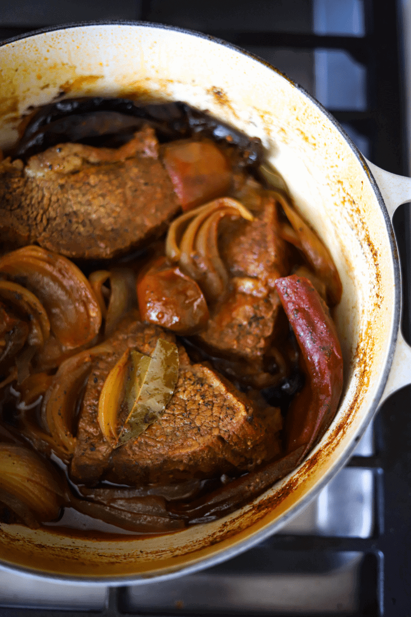 Stewed guajillo and pasilla peppers, beef roast, quartered onions and tomatoes in preparation for making Mexican birria