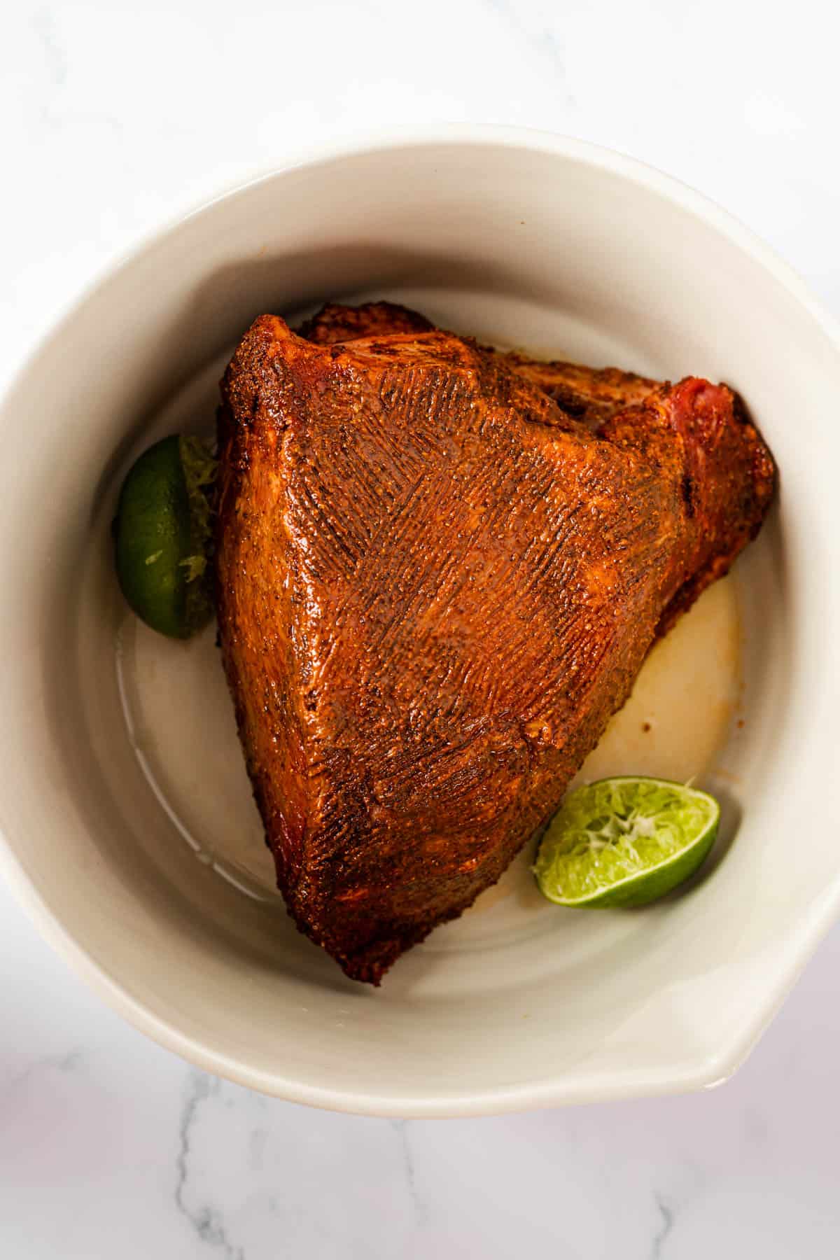 seasoned bottom round roast in a bowl with squeezed lime halves