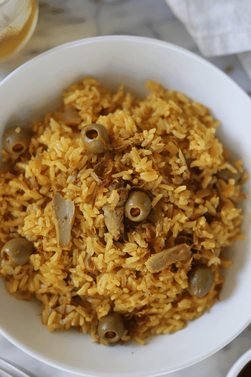 This is a close-up photo of Cape Verdean rice with tuna (arroz de atum) presented in a bowl with a napkin and beverage off to the side