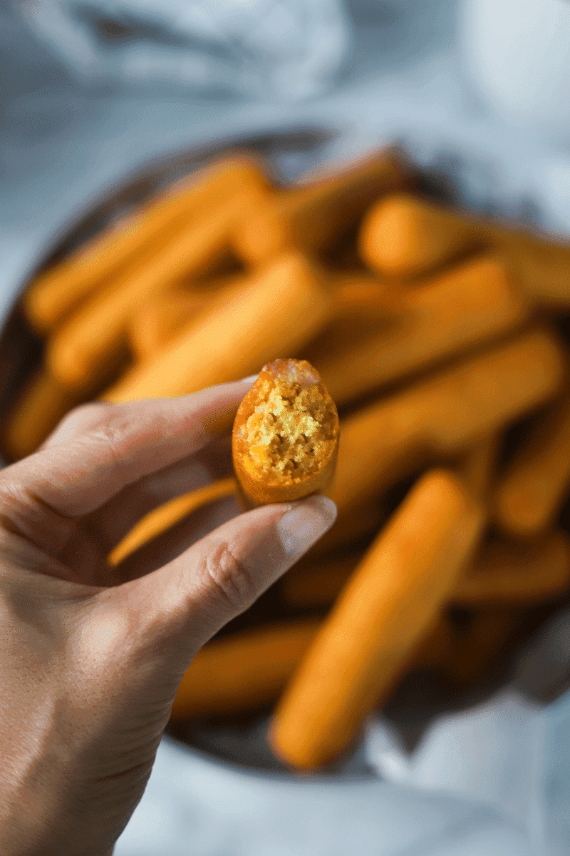 Close up photo of a single Cape Verdean gufong that's been bitten to show the texture of the inside. The author is holding it in her hand and there is a plate of gufong in the background.