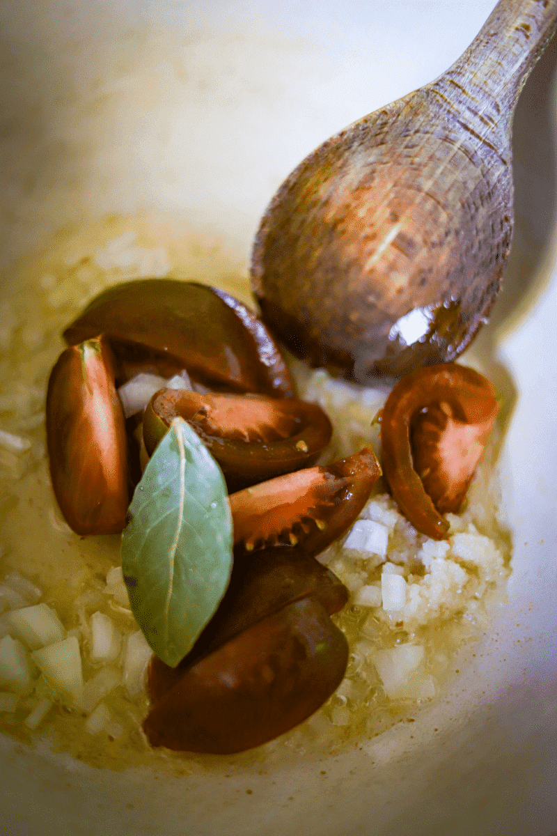 close up photo displays garlic, onions, bay leaf and tomatoes being cooked