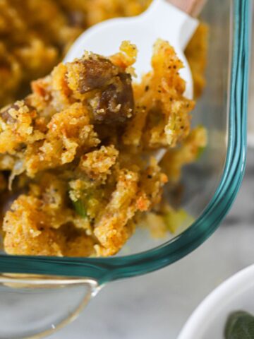baked cornbread stuffing in a glass baking dish scooped with a spoon.