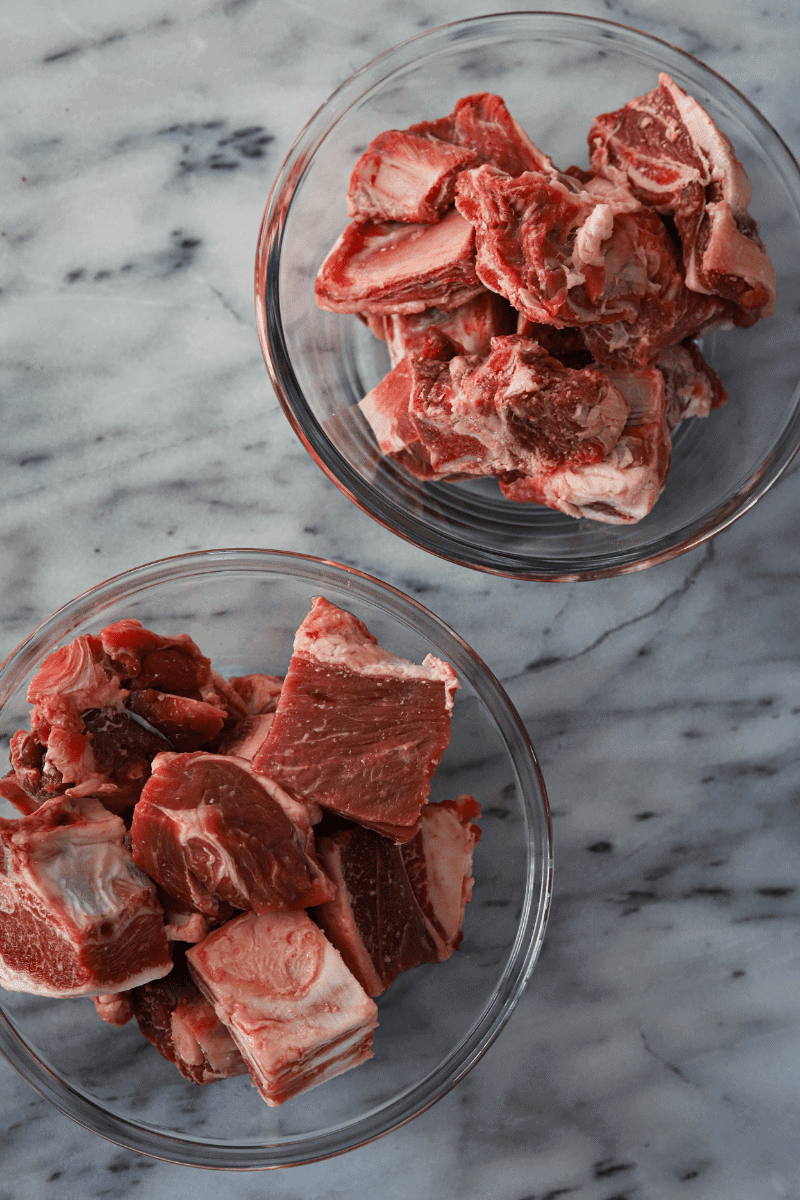 This is a close up photo of 1 bowl of lamb stew meat and another bowl of cubed goat meat.