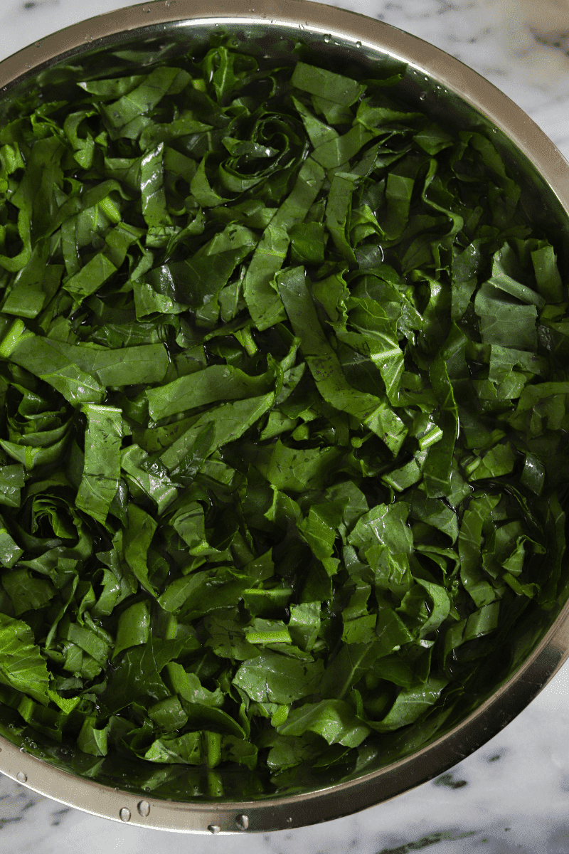 This is a photo of chopped collard greens soaking in a large metal bowl of water