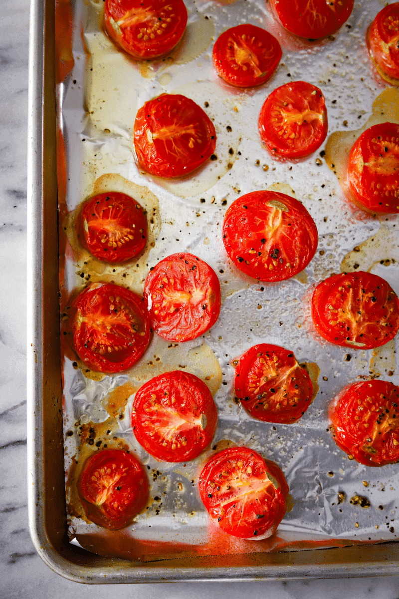 Sliced roasted campari tomatoes on a foil-lined baking sheet. The tomatoes are drizzled in olive oil and sprinkled with kosher salt and pepper.