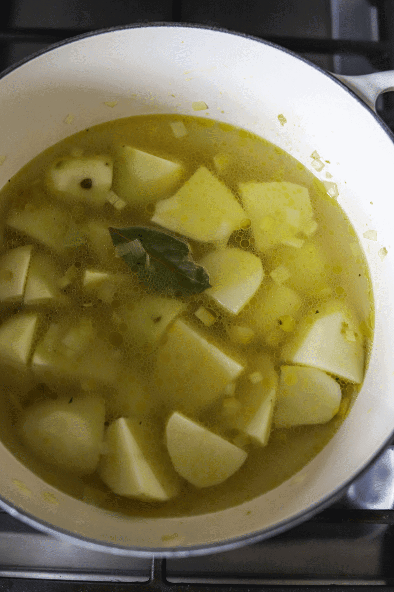 This photo shows the quartered potatoes, bay leaf and onions covered in water in a soup pot.
