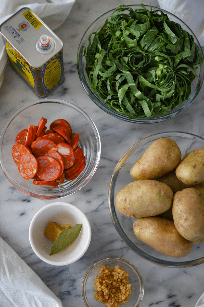 This photo shows the key ingredients needed to make Portuguese-style caldo verde: olive oil, thinly shredded collard greens, potatoes, minced garlic, bouillon cubes and a bay leaf