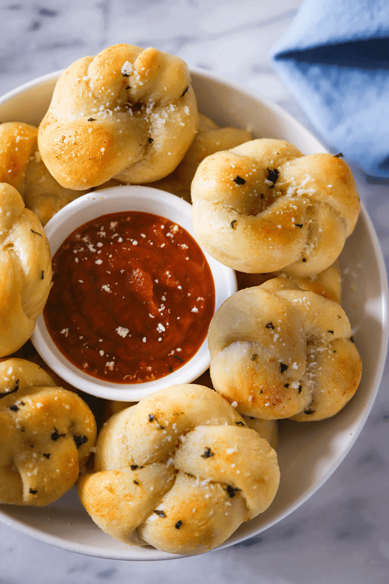 This is a bowl of garlic knots that have been brushed in garlic butter and sprinkled with grated parmesan cheese