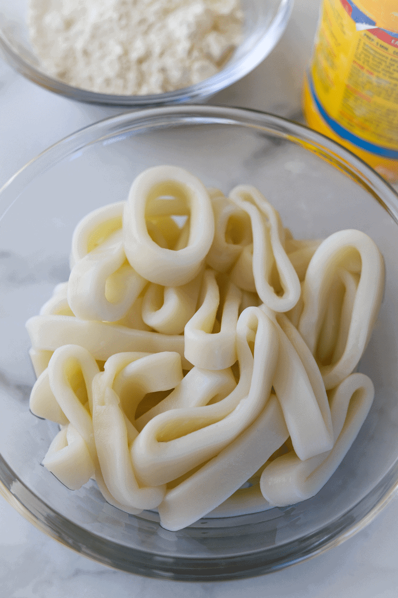 close up photo of cleaned squid rings with cornstarch container and bowl of flour in the background
