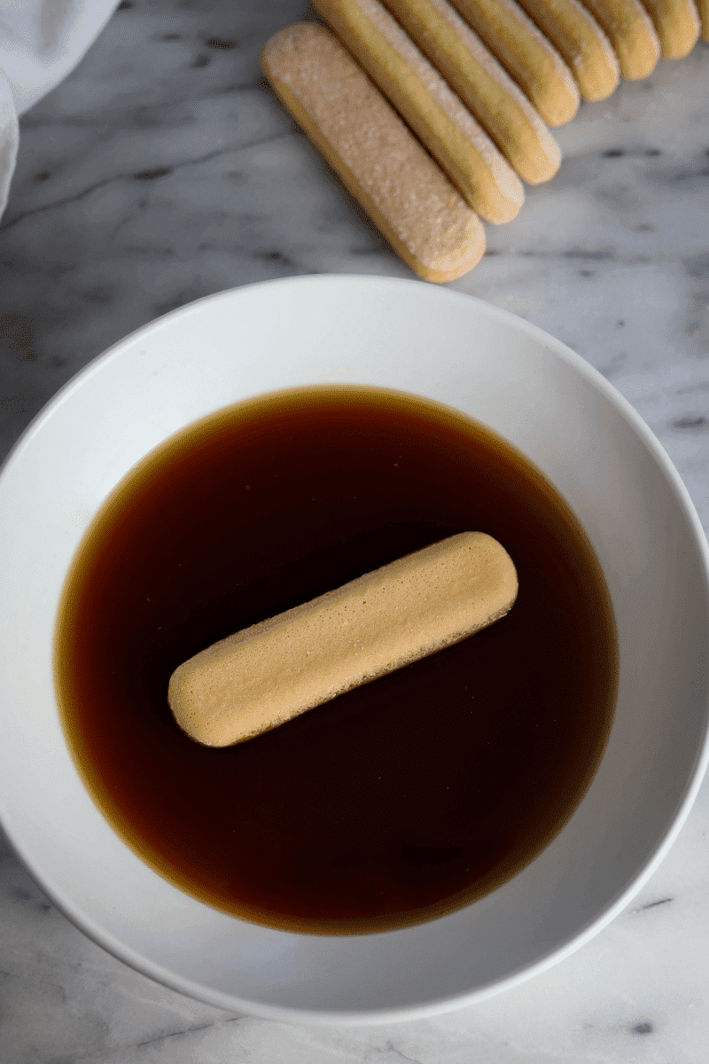 easy tiramisu recipe-process shot demonstrates ladyfinger being dipped in espresso