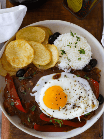 overhead shot of bitoque (portuguese steak) topped with egg and served with rice and fried potatoes