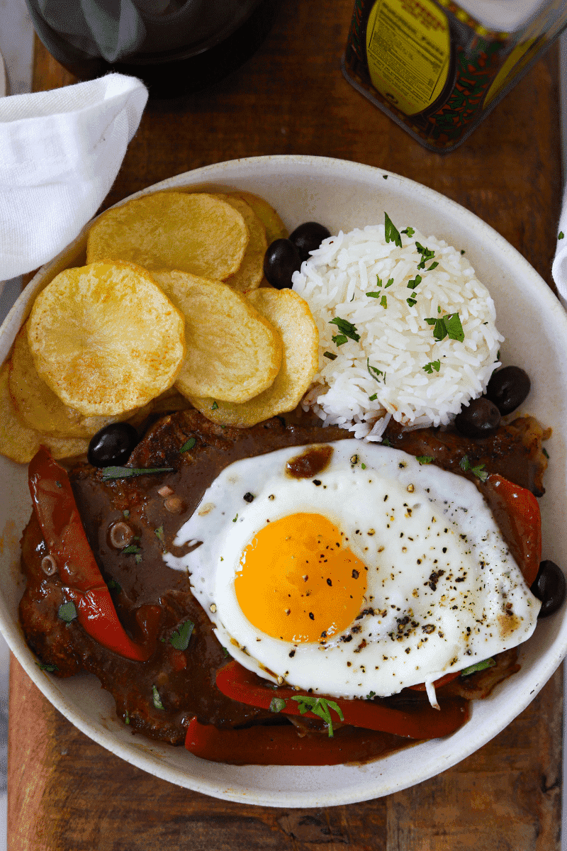 overhead shot of bitoque (portuguese steak) topped with egg and served with rice and fried potatoes