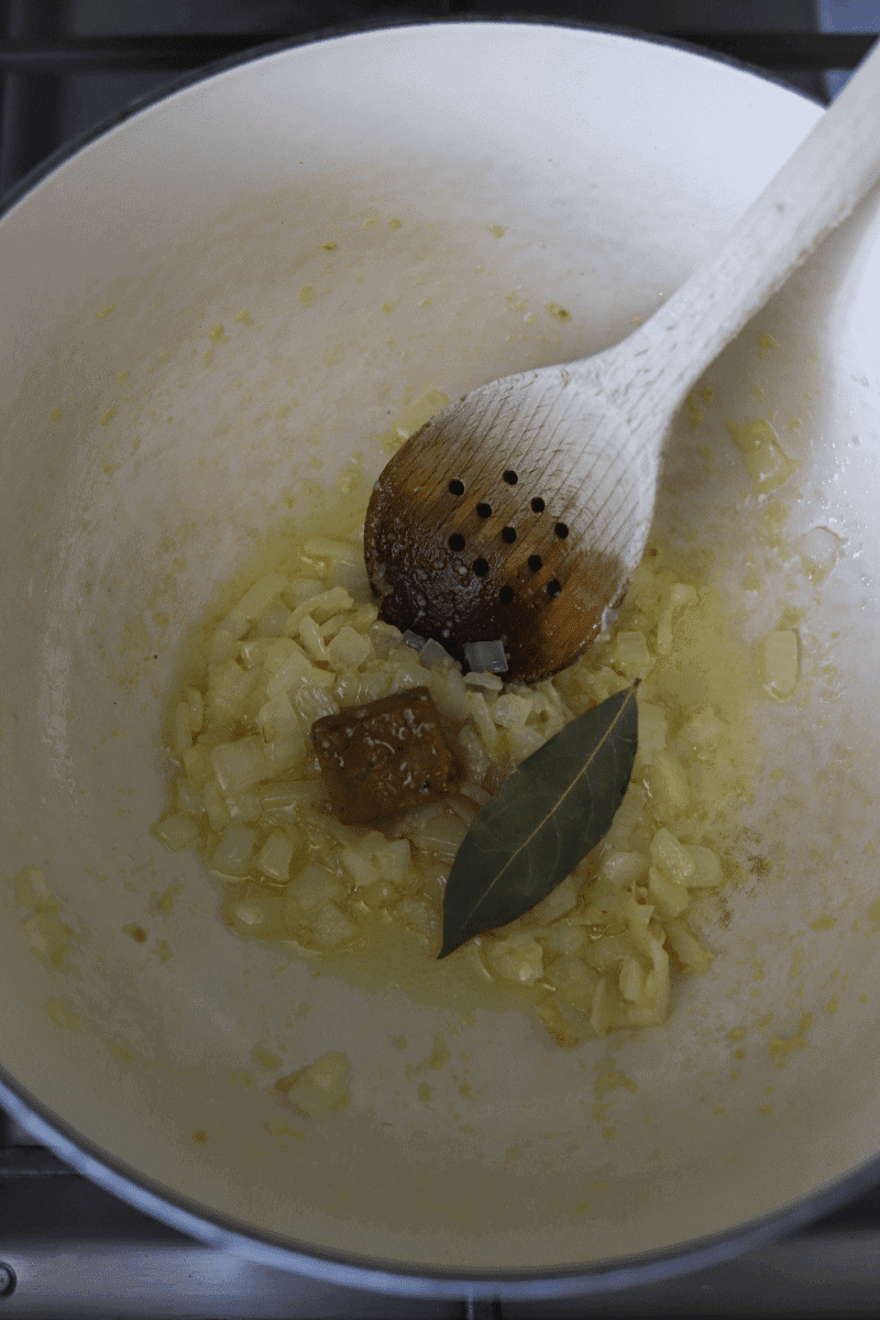 sauteed onions, bouillon cube and bay leaf in a pan in preparation for Cape Verdean style rice with lima beans