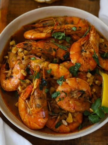 shrimp mozambique shown in dish garnished with lemon and cilantro