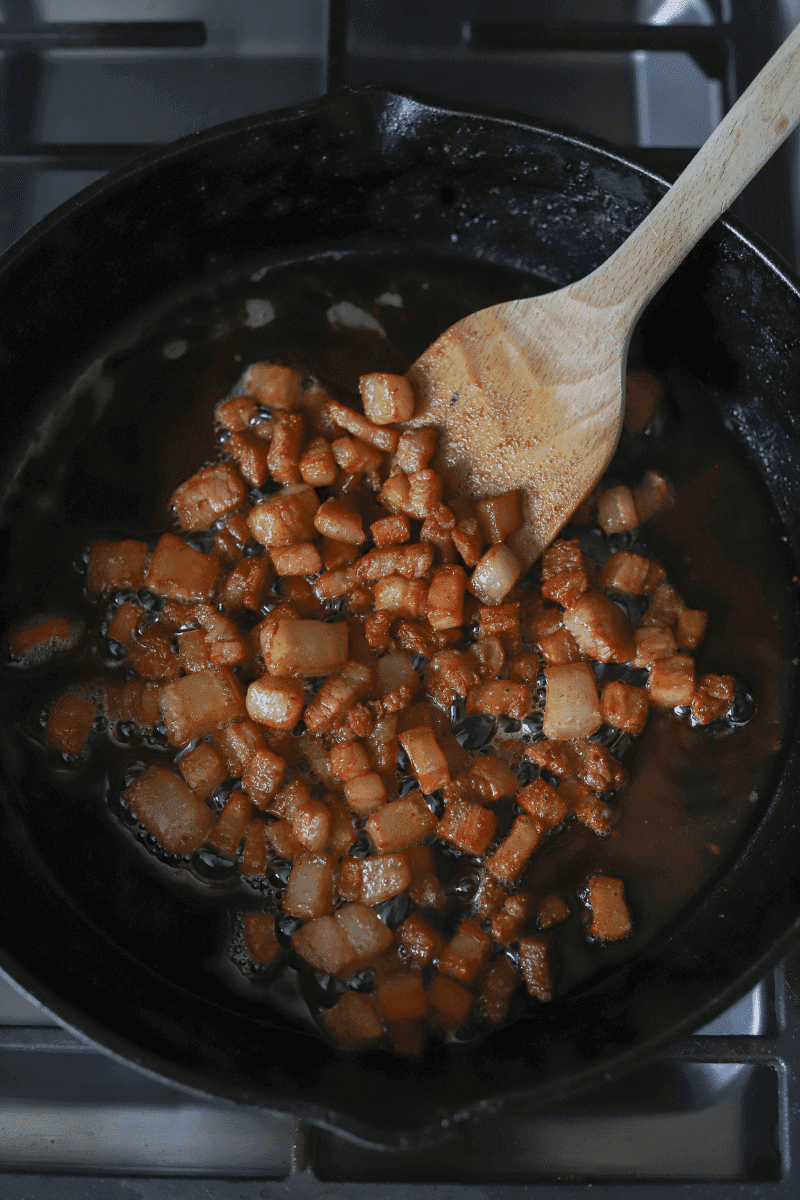 process shot of salt pork being browned in a skillet