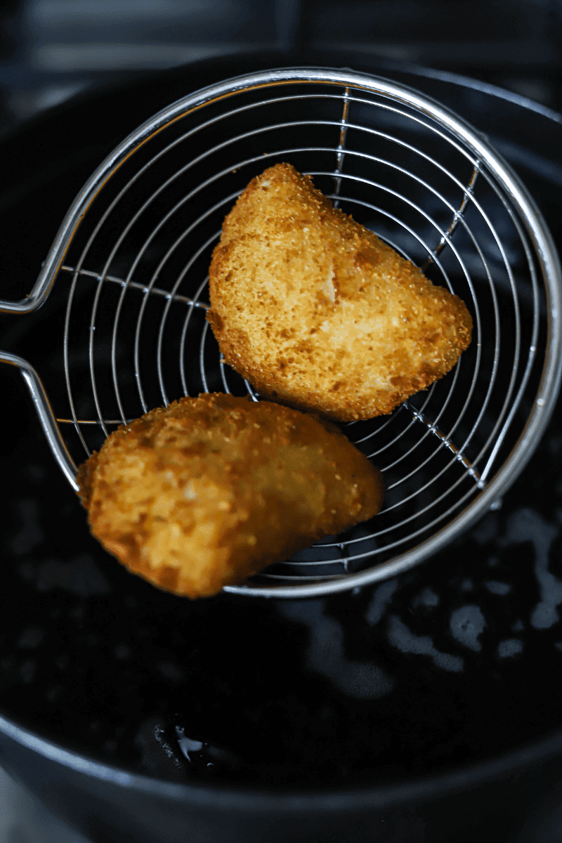 process shot of fried tuna rissois being lifted out of the frying oil on a spider strainer