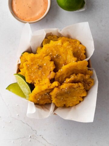 Fried green plantains (tostones) sprinkled with salt. Shown with limes and mayoketchup dipping sauce