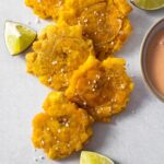 Fried green plantains (tostones) sprinkled with salt and served with lime wedges and mayo ketchup dipping sauce