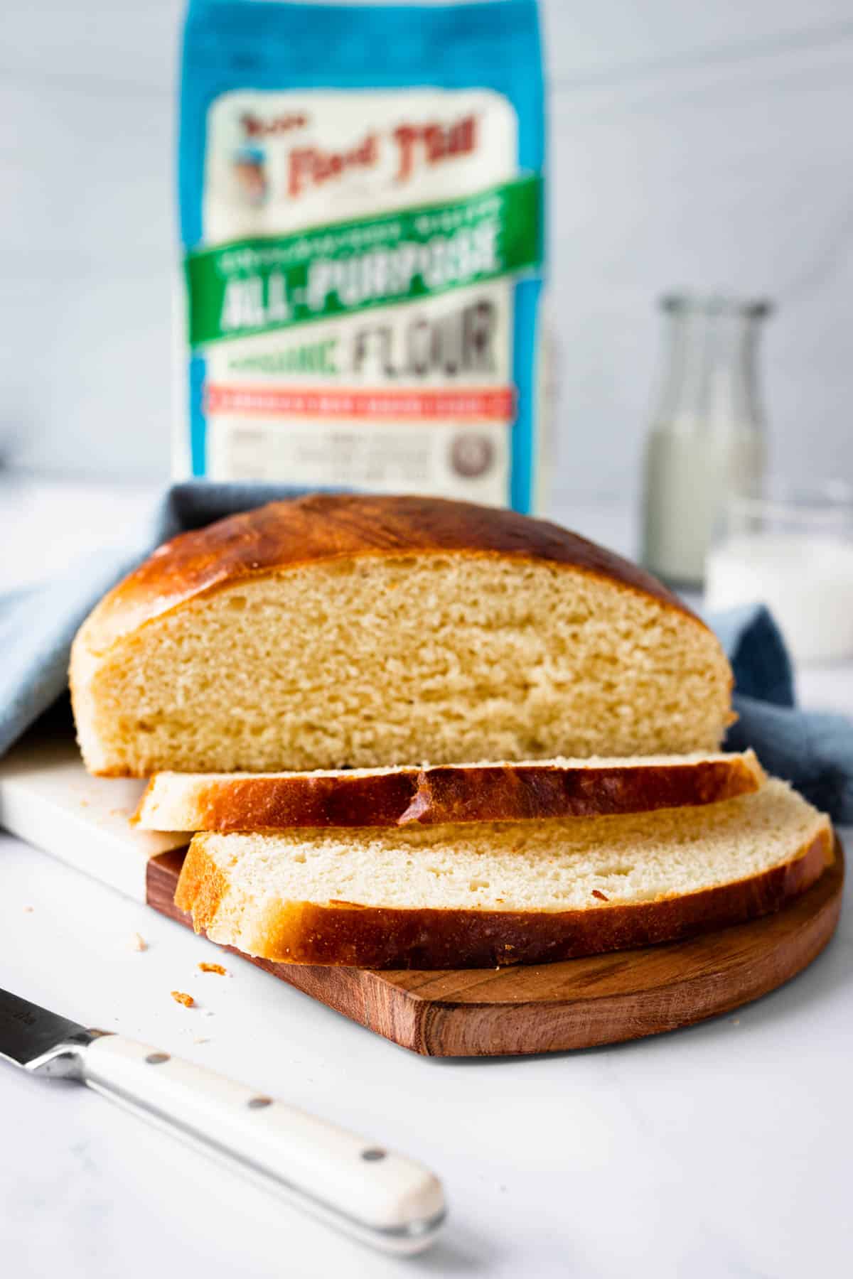 Loaf of baked, sliced Portuguese sweet bread with Bob's Red Mill flour in background.