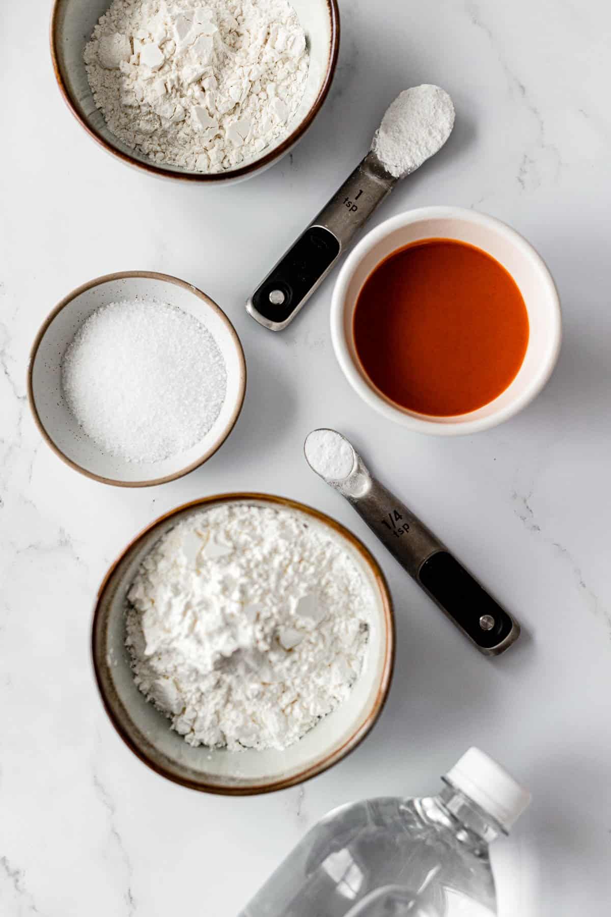 Supporting ingredients for vegan buffalo cauliflower, listed from top to bottom: flour, baking powder, buffalo sauce, kosher salt, cornstarch, club soda. Cauliflower not shown.