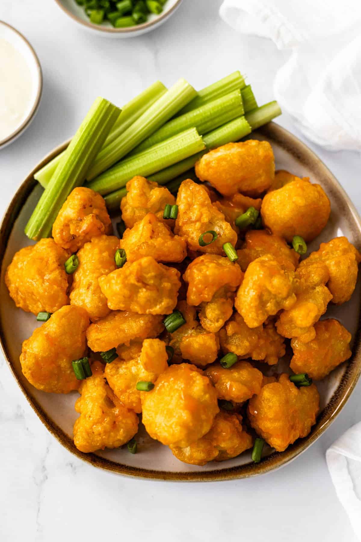 Plate of vegan buffalo cauliflower wings garnished with celery and green onions