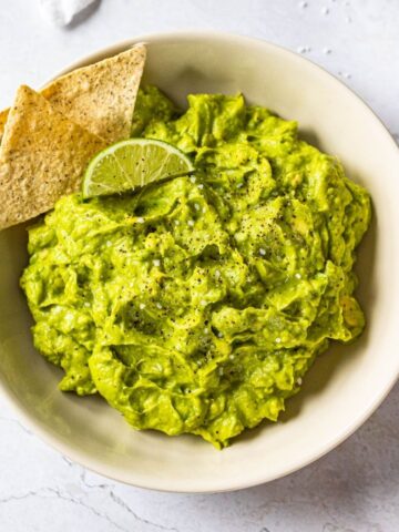 bowl of guacamole with tortilla chips and lime wedges