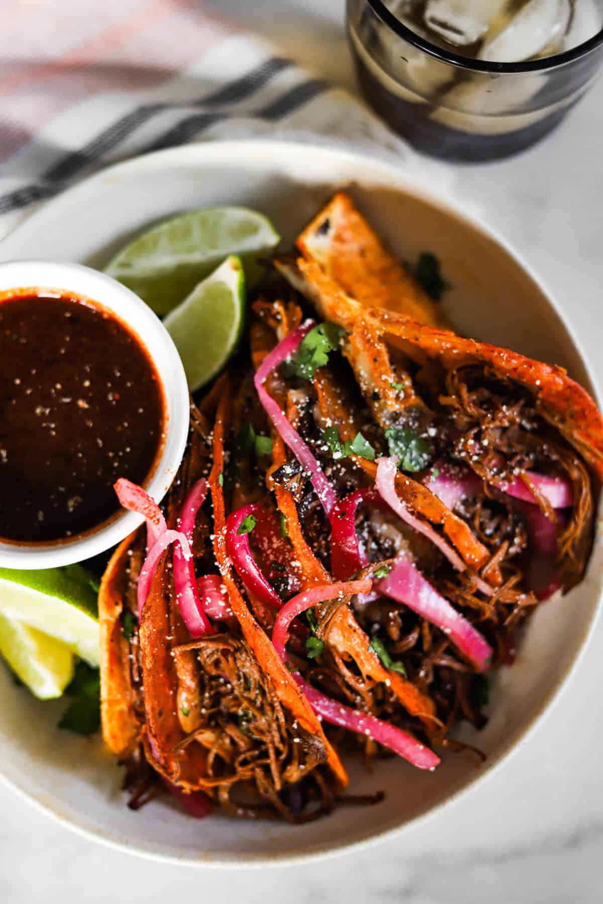 Birria tacos with a dipping bowl of consomme and fresh lime wedges