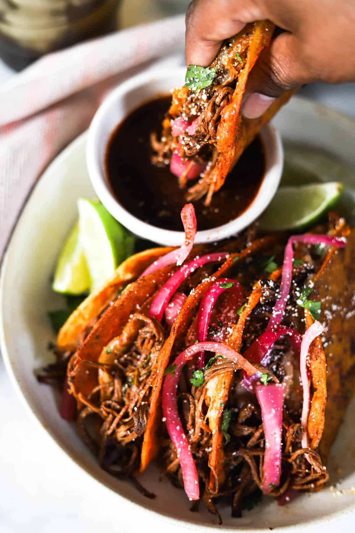 Birria tacos on a plate being dipped in consomme