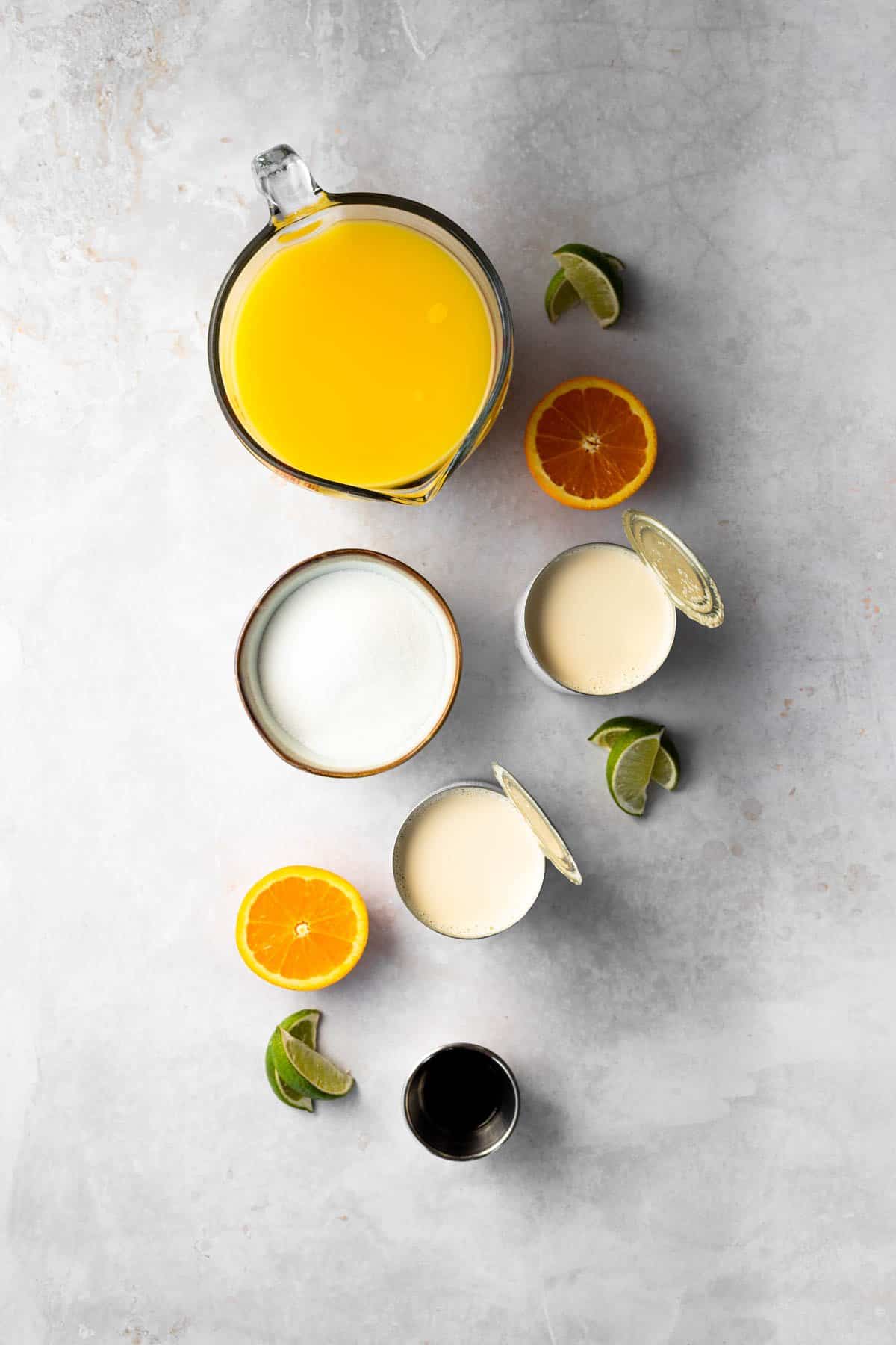 ingredients for making morir soñando - orange juice, 2 cans evaporated milk, granulated sugar, lime and vanilla extract. Oranges shown for decoration